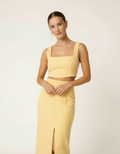 Modelo posando com conjunto cropped e saia midi amarelo manteiga, mãos juntas frente - Amarine