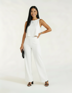 Mulher posando com mão na cintura usando conjunto branco de blusa cropped e calça wide leg, bolsa preta clutch e sandália preta