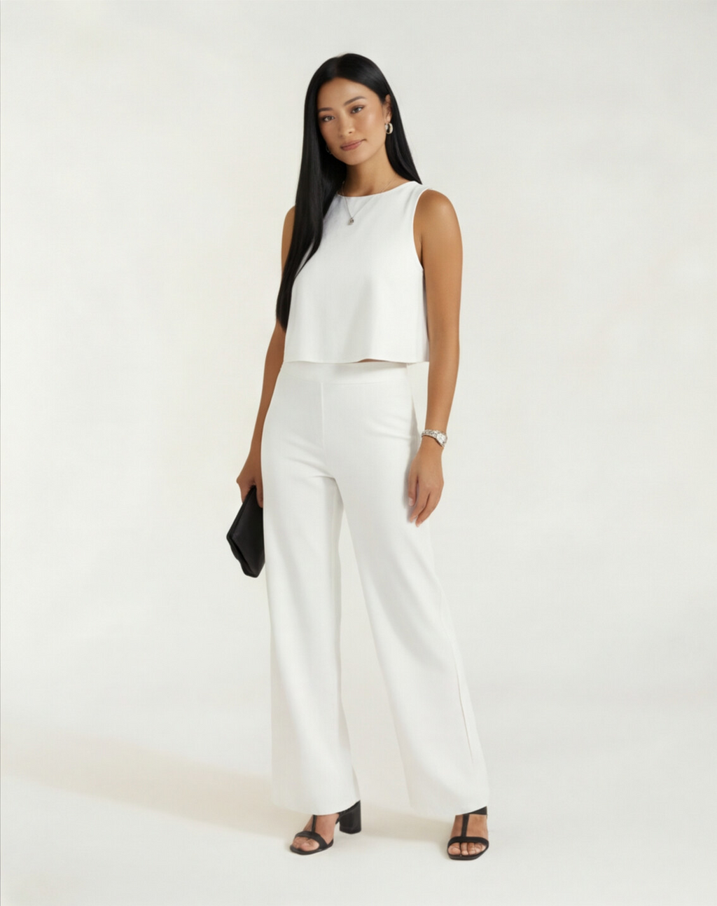 Mulher de corpo inteiro com conjunto branco de blusa cropped e calça wide leg, bolsa preta clutch e sandália preta