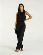 Mulher com conjunto preto de blusa e calça wide leg, segurando bolsa preta clutch e sandália preta de salto
