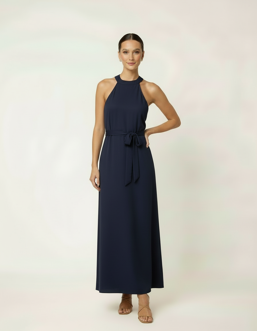 Mulher de frente com vestido halter longo azul marinho com cinto laço e sandália rasteira bege