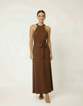 Mulher de frente com vestido halter longo marrom com cinto laço e sandália rasteira feminina
