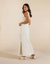 Mulher de lado com vestido longo branco com fenda lateral e sandália branca de salto