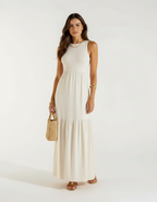 Mulher com vestido longo branco off-white com saia rodada, bolsa de palha rattan e sandália bege