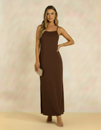 Mulher posando com vestido longo marrom de alças finas com bolsa clutch dourada e sandália