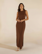 Mulher de frente com vestido longo marrom chocolate com fenda lateral e sandália branca rasteira