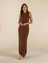Mulher de frente com vestido longo marrom chocolate com fenda lateral e sandália branca rasteira