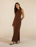 Mulher de pé com vestido longo marrom chocolate com fenda lateral e sandália branca rasteira chunky