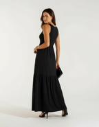 Mulher de lado com vestido longo preto com saia rodada, bolsa preta e sandália preta de salto