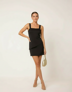 Mulher com vestido curto preto de alça larga estilo bodycon com bolsa e sandália dourada