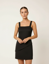 Mulher de frente com vestido curto preto de alça larga estilo bodycon com mãos à frente